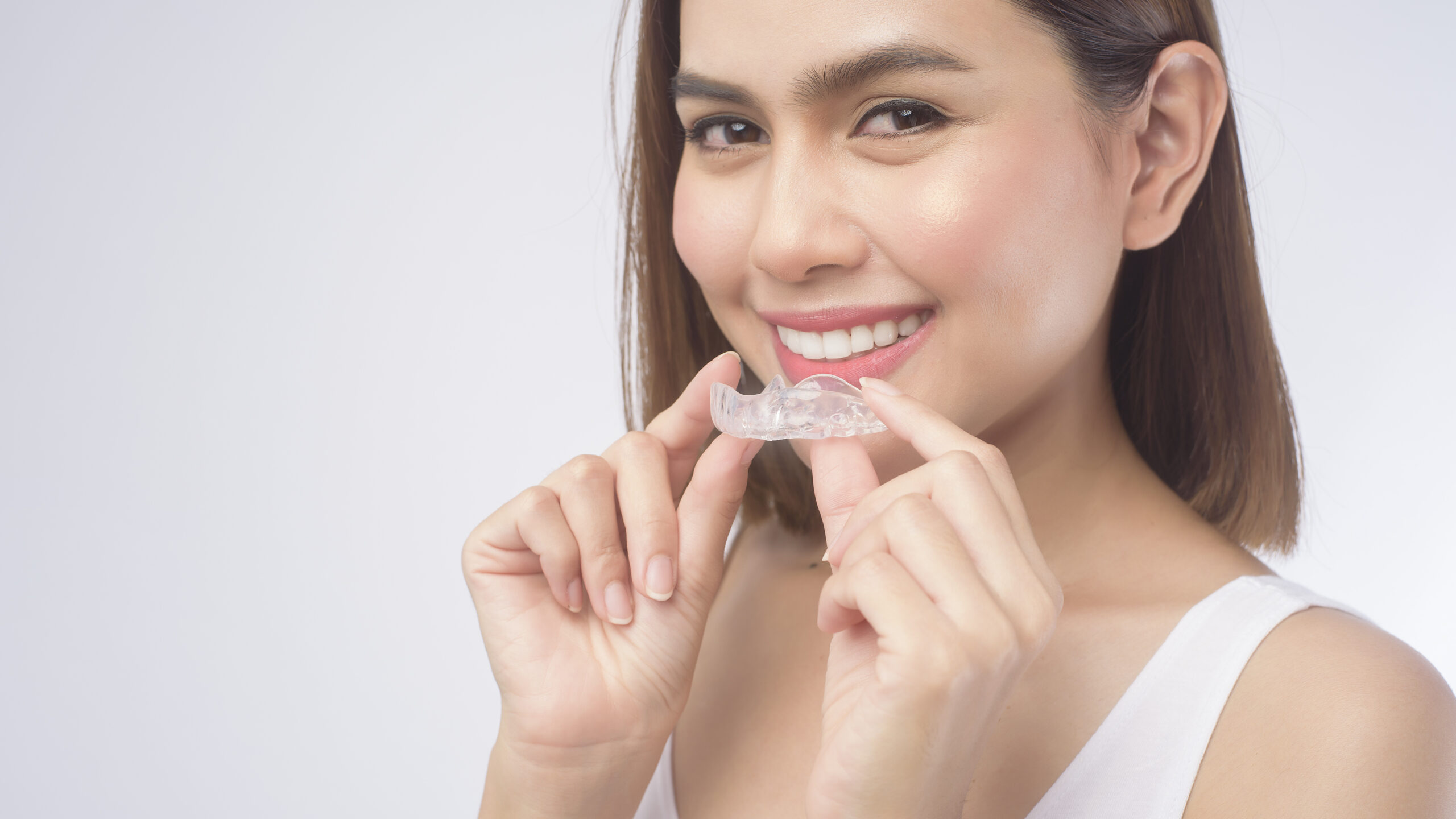 Smiling woman holding a clear Invisalign retainer to prevent orthodontic relapse