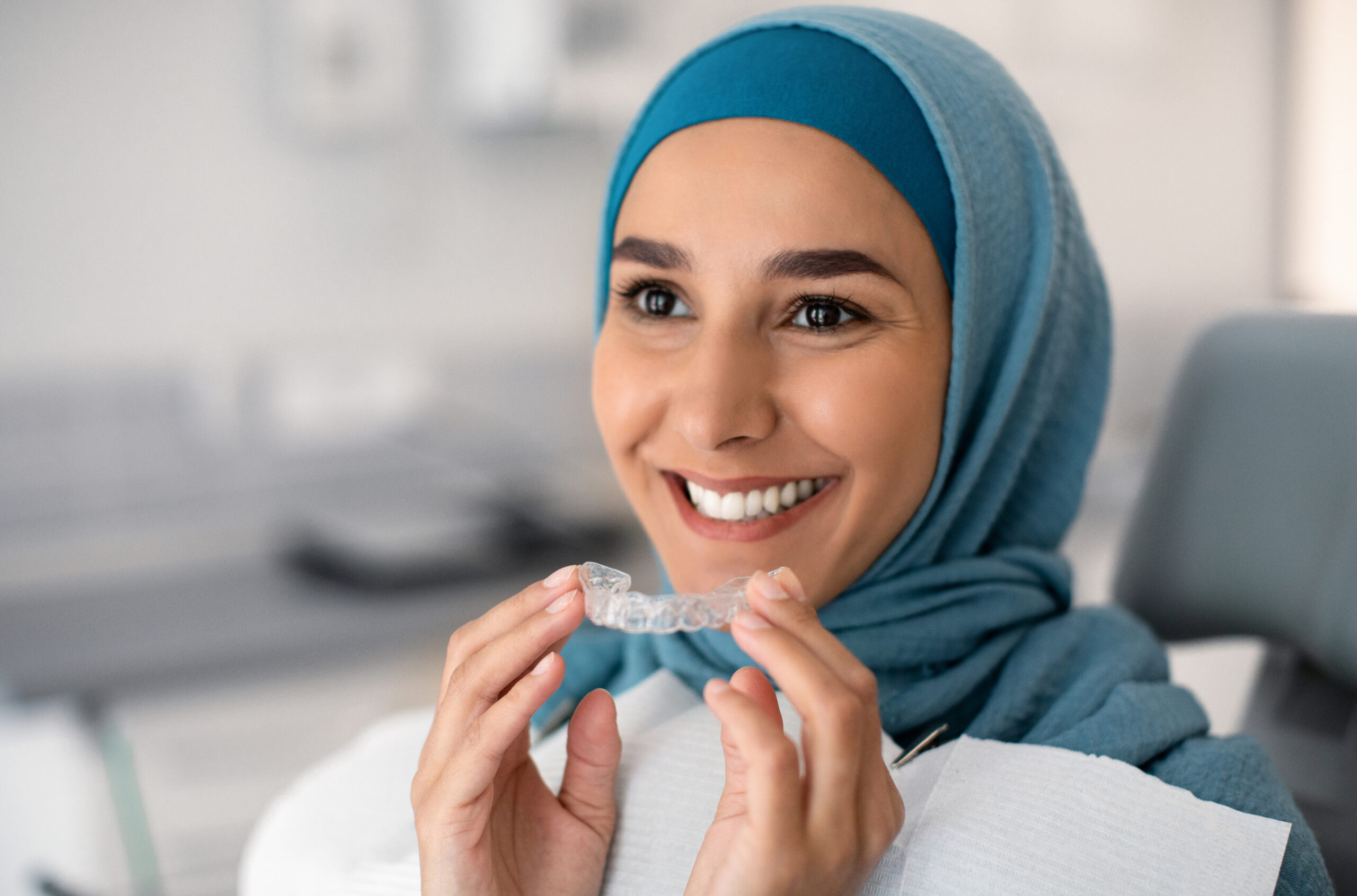 Smiling woman holding a clear Invisalign aligner during a dental consultation